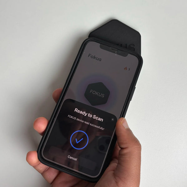 Hand holding a smartphone with Fokus app on a light gray background