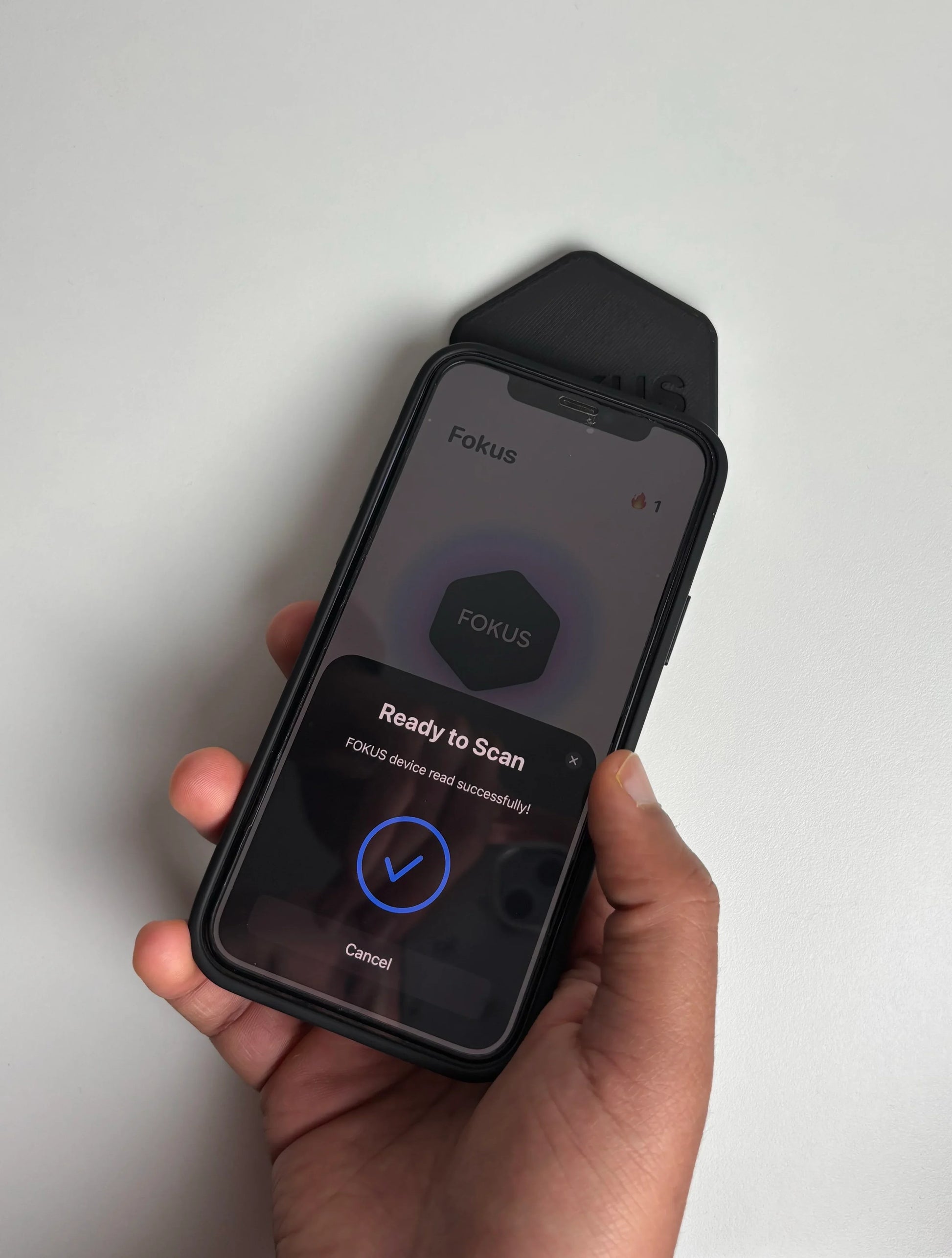 Hand holding a smartphone with Fokus app on a light gray background